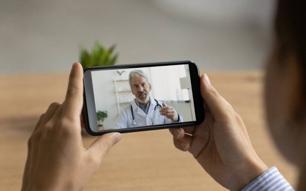 Woman's hands holding a mobile with a doctor on the screen offering a medical consultation