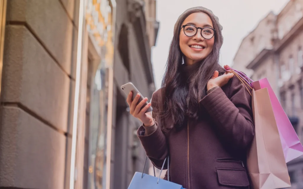 Woman carrying a shopping bag and holding a mobile as she enjoys her eGifting