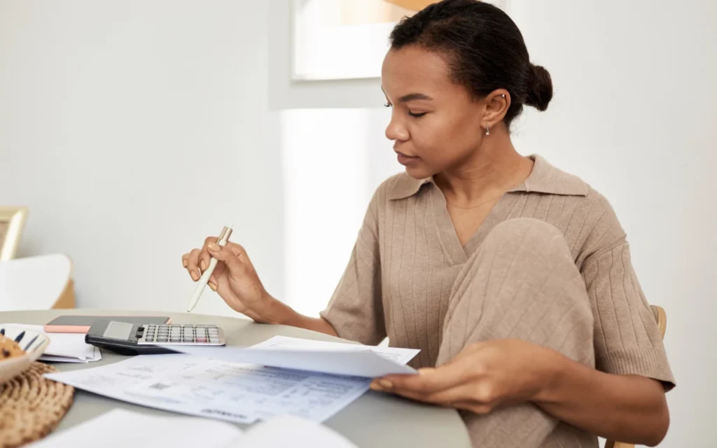 A woman sitting with a pile of papers using a calculator