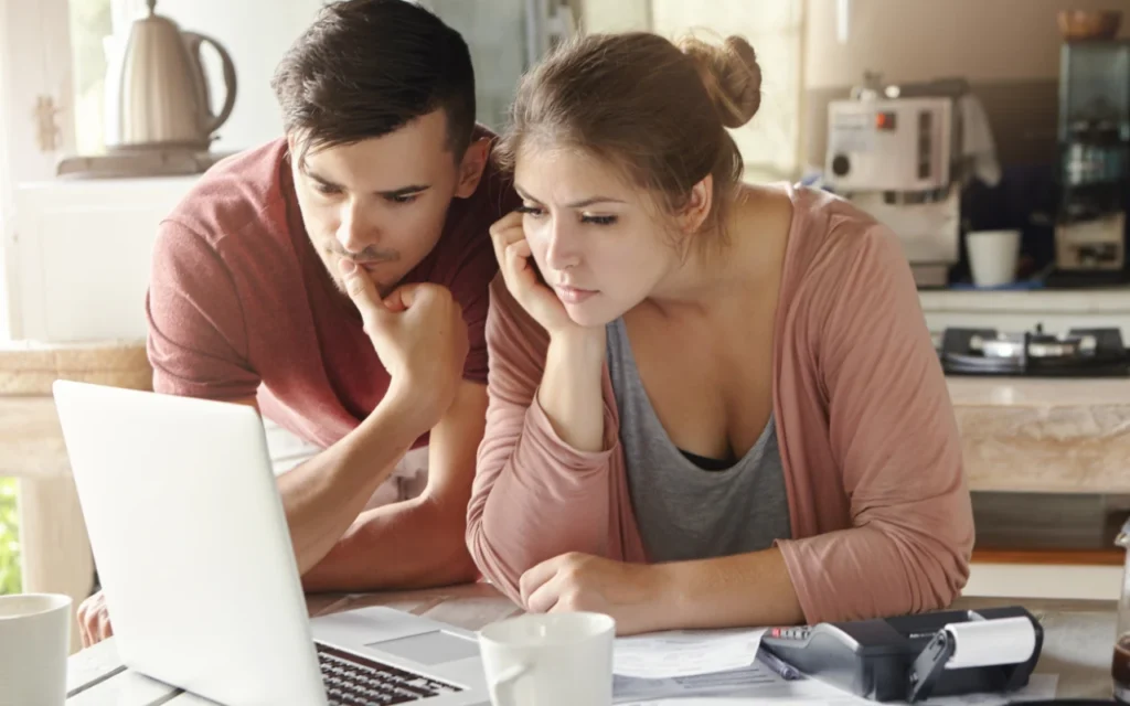 man and woman sitting together in front of a laptop looking thoughtful