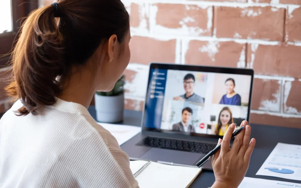 a woman waves at her colleagues on a laptop during a company meeting
