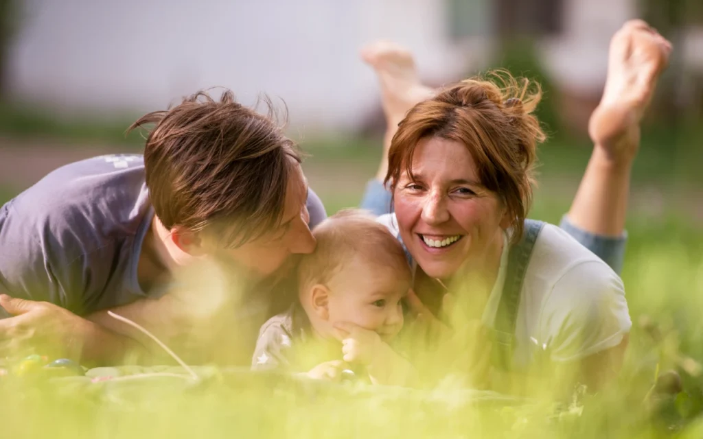 Young couple with their toddler lying in long grass in the sunshine