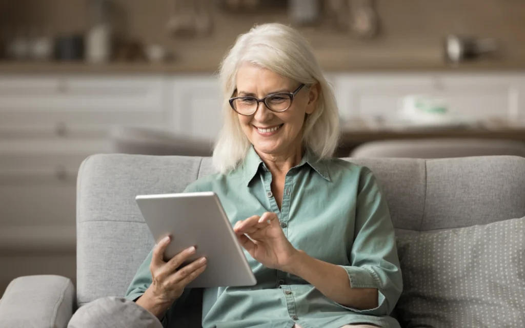 Woman sitting on a sofa using a tablet and smiling - part of the Tech Benefits