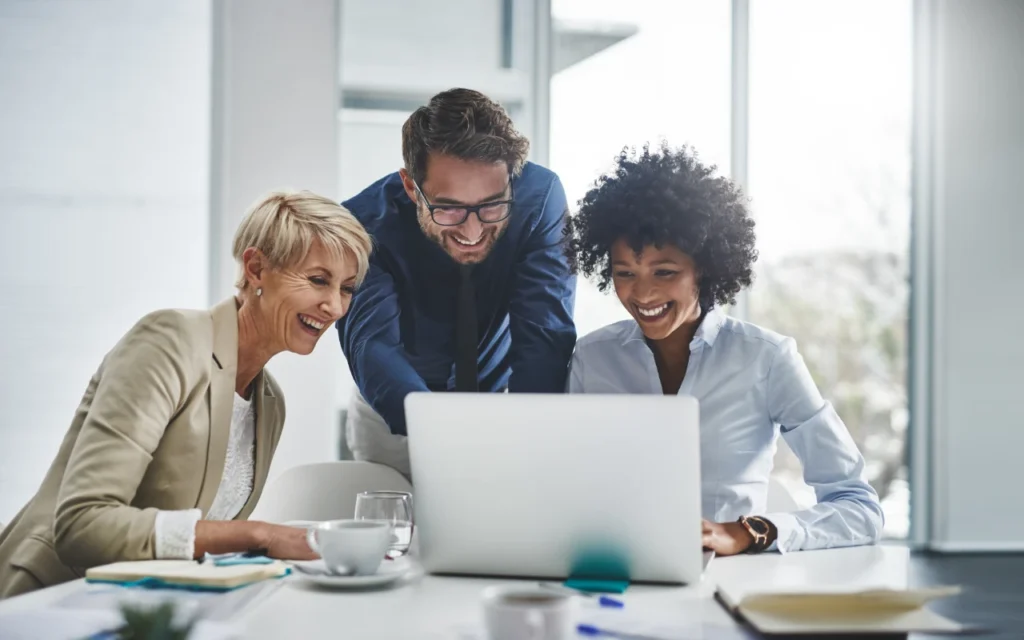 three employees gathering around a laptop comparing employee benefits providers in the uk