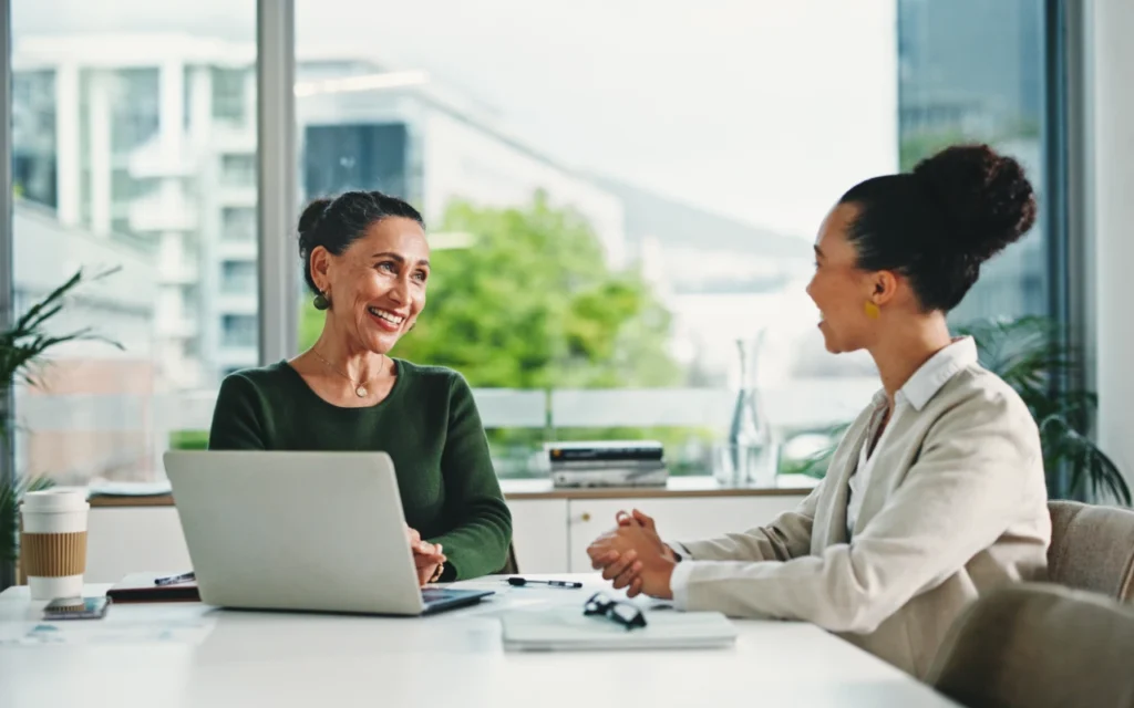 two women sat at an office table discussing the pros and cons of in-house vs outsourced employee benefits administration